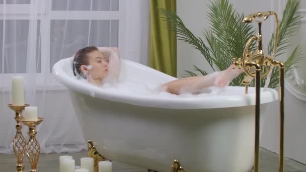 Красивая женщина отдыхает в ванне с пеной, лежащей в ванной. Концепция красоты, активного отдыха и здравоохранения
 - Кадры, видео