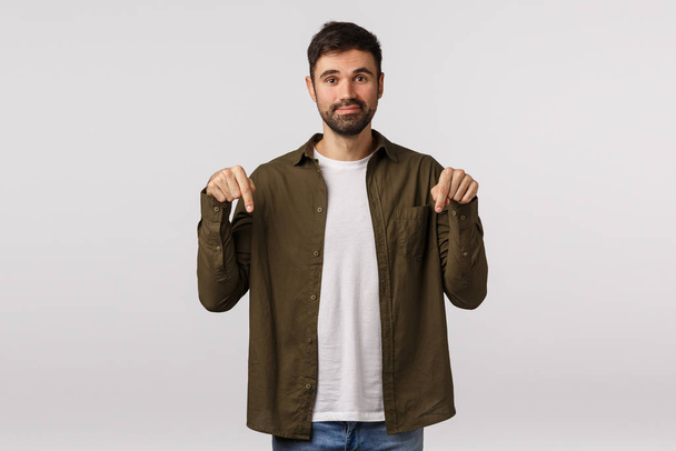 Better check this out and buy. Cute and friendly modern bearded caucasian male in coat, pointing down to turn attention corporate promo, give advice recommend visit shopping site, white background - Photo, Image