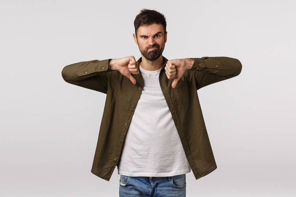 Wrong choice, totally dislike it. Displeased and unsatisfied male customer leave negative feedback, show thumbs-down, grimacing unhappy and disappointed, standing white background upset - Fotoğraf, Görsel