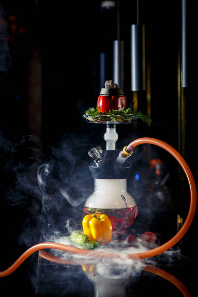 Hookah on vegetables. Hookah  flask contains chopped vegetables: pepper, cucumber, radishes, herbs. Vegetables are filled with red liquor. Bowl of red pepper hookah. Lots of smoke. - Fotografie, Obrázek