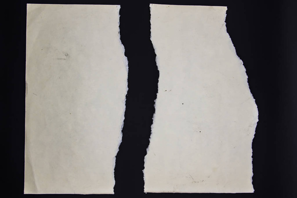 Een gescheurd vel papier op een zwarte achtergrond - Foto, afbeelding