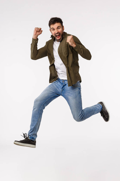 Achievement, congratulations and business concept. Full-length studio vertical shot attractive cheerful man jumping from triumph and celebration, achieve goal, win prize, clench arms pleased - Foto, immagini