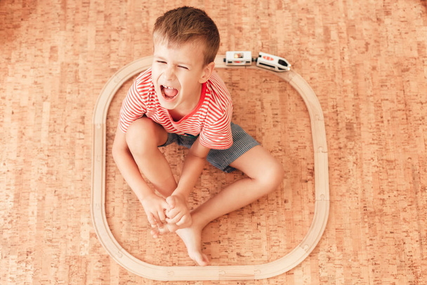 Adorable boy sitting on floor with wooden railway around him - Foto, afbeelding