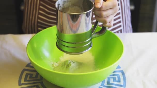 Close-up of a female hand sifting flour with a sieve mug in a green bowl in the home kitchen. Cooking pancakes - Séquence, vidéo