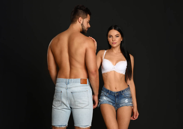 Young woman in underwear and denim shorts with her boyfriend on black background - Fotoğraf, Görsel