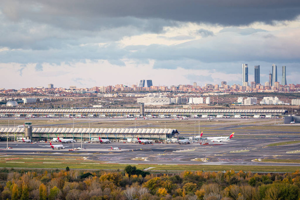 Μαδρίτη, Ισπανία; 11 / 23 / 2019: Ανατολή ηλίου στο αεροδρόμιο Adolfo Suarez Μαδρίτη Barajas με θέα τον ορίζοντα της πόλης και τους "τέσσερις πύργους" με συννεφιασμένο ουρανό - Φωτογραφία, εικόνα