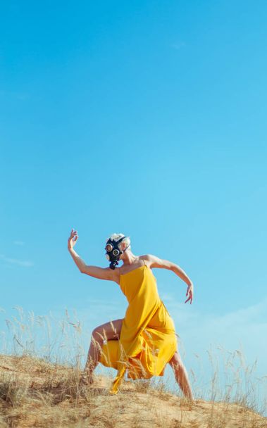 Girls in yellow dress and Gasmask dancing on the sand dunes - Foto, afbeelding