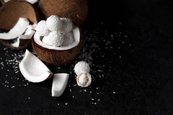 cooked coconut milk candies on a black dark background, ingredients for a dessert with coconuts, a sweet product with coconut flakes - Fotoğraf, Görsel