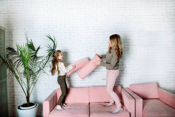 Parental love, upbringing and care.Happy mommy and kid daughter holding hands jumping on sofa together, baby sitter or mother playing having fun with cute kid girl at home - Photo, Image