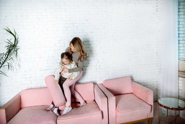 Parental love, upbringing and care.Happy mommy and kid daughter holding hands jumping on sofa together, baby sitter or mother playing having fun with cute kid girl at home - Fotografie, Obrázek