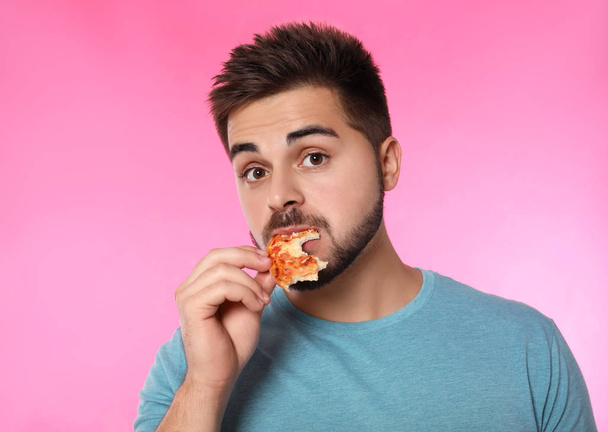 Emotional man eating pizza on pink background - Фото, зображення