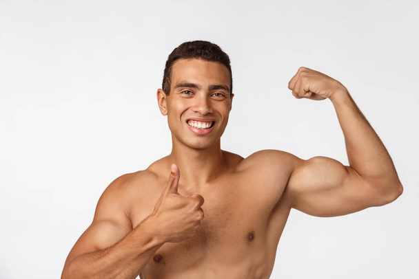 Adolescente afro-americano mostra músculos no braço. Isolado em fundo branco. Retrato de estúdio. Conceito de idade transitória
. - Foto, Imagem