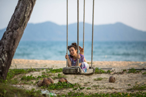 Μικτή φυλετική κοπέλα αιωρείται σε μια κούνια σε μια τροπική παραλία. - Φωτογραφία, εικόνα