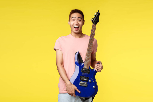 Handsome young musician playing the guitar and singing, isolated on yellow background - Photo, Image