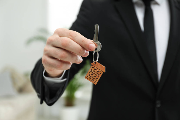 Агент по недвижимости держит ключ от дома с безделушкой в помещении, крупный план
 - Фото, изображение