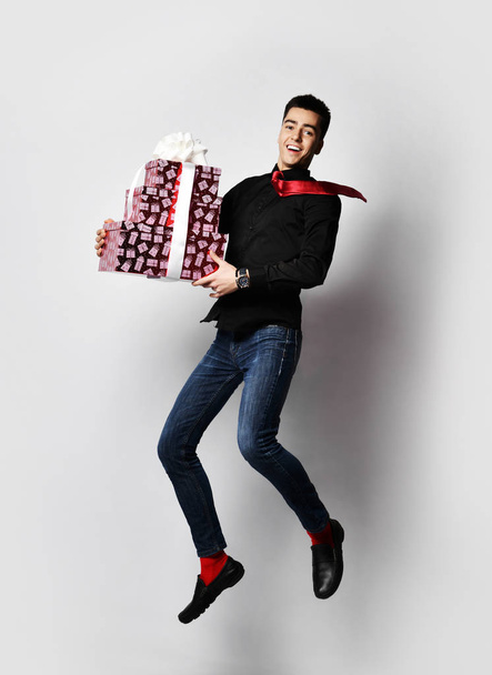 Young handsome guy is in a hurry for a Christmas dinner with a bunch of New Year red gift boxes presents - Photo, image