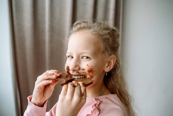 Little girl eating chocolate. a little girl smeared chocolate. a sweet chocolate holiday. dirty hands and cheeks. face in chocolate - Foto, imagen