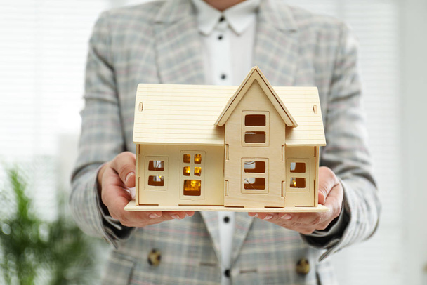 Real estate agent holding wooden house model with lights indoors, closeup - Foto, Imagem