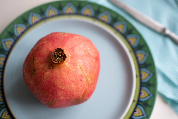Large ripe pomegranate on a turquoise plate with a metal knife on a plaid napkin - Photo, Image