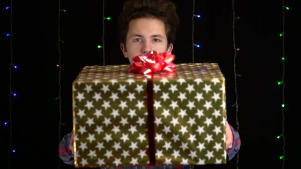 chlapec s dárkovou krabicí na černém pozadí. dárková krabička se stuhou na Šťastný Nový rok, Veselé Vánoce, Valentýn, narozeniny - Záběry, video