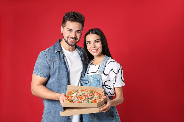 Happy young couple with pizza on red background - Foto, Imagem