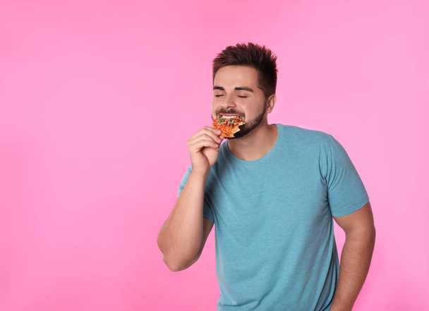 Handsome man eating pizza on pink background, space for text - Photo, image