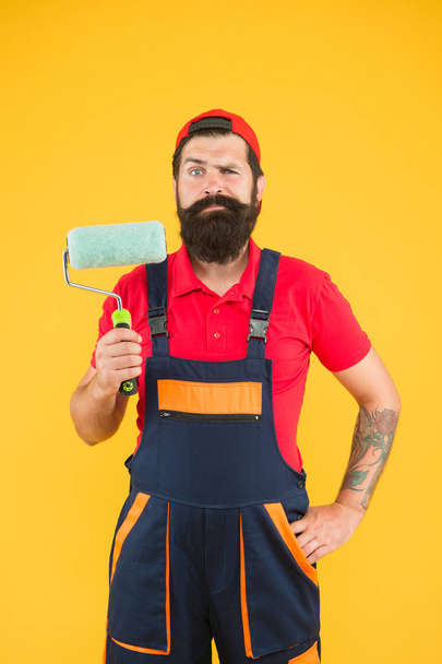 making house renovation. hipster builder in cap yellow background. erector assistant in work uniform. engineer designer ready to paint wall. repair concept. bearded man worker with roller tool - Foto, Imagen