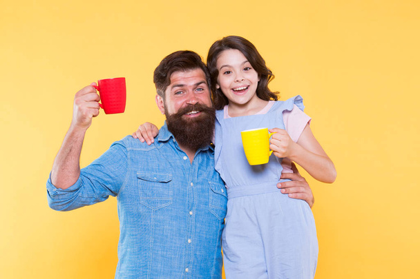 Drink water. Drink fresh juice. Breakfast concept. Good morning. Having coffee together. Healthy lifestyle. Family drinking tea. Bearded man and happy girl holding mugs. Father and daughter hot drink - Photo, image