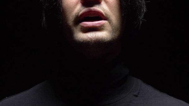 Een close-up. mannelijke mond met kromme tanden schreeuwend. Zwarte achtergrond. - Foto, afbeelding