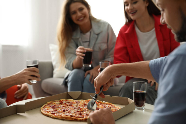 Man cutting fresh pizza on table and friends indoors, closeup - Photo, image