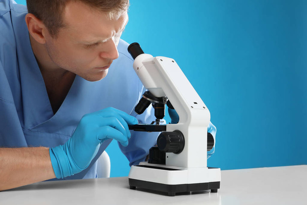 Vědec pomocí moderního mikroskopu u stolu proti modrému pozadí - Fotografie, Obrázek