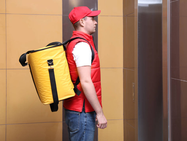 Correio masculino com saco térmico à espera de elevador. Serviço de entrega de alimentos
 - Foto, Imagem