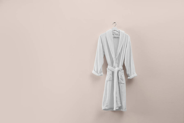 Soft comfortable bathrobe hanging on beige wall, space for text - Fotoğraf, Görsel