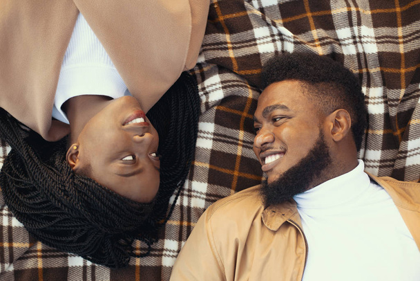 Vista superior de pareja afro romántico tumbado en picnic a cuadros al aire libre
 - Foto, Imagen