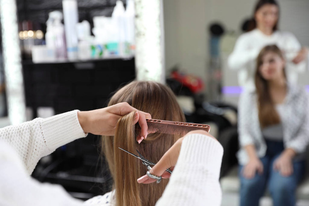 Hairdresser making stylish haircut with professional scissors in salon, closeup - 写真・画像