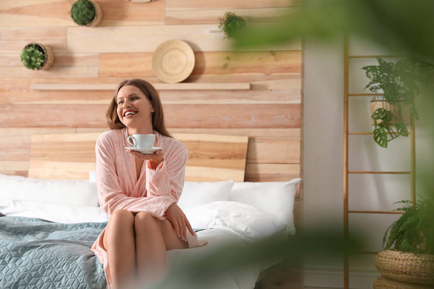 Woman drinking coffee in bedroom with green plants. Home design  - Фото, изображение