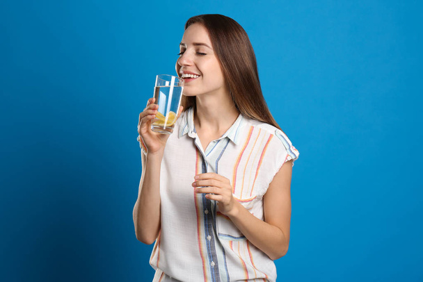 Young woman drinking lemon water on light blue background - Fotografie, Obrázek