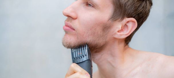 közeli kép fiatal férfi személy vágás a szakáll segítségével a trimmer - Fotó, kép