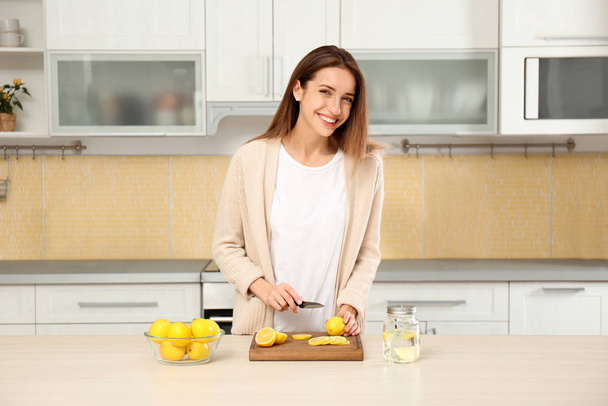 Young woman making lemon water in kitchen - Fotó, kép