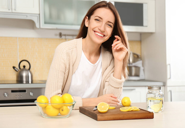 Young woman making lemon water in kitchen - Zdjęcie, obraz