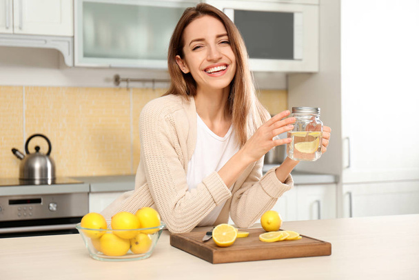 Young woman with mason jar of lemon water in kitchen - Valokuva, kuva