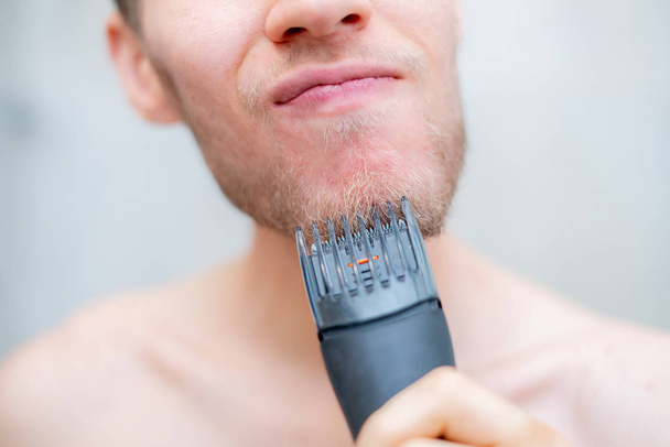close up de jovem homem pessoa cortando sua barba usando o aparador - Foto, Imagem