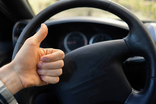 first person view of driver showing thumb up in front of steering wheel - Foto, Imagen