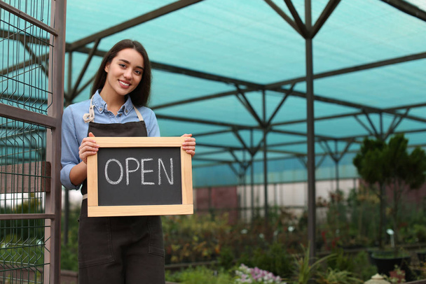 Female business owner holding OPEN sign in greenhouse. Space for text - Fotoğraf, Görsel