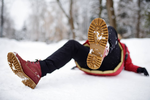 Shot of person during falling in snowy winter park. Woman slip on the icy path, fell and lies. - Foto, afbeelding
