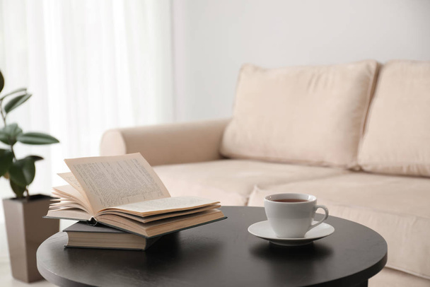 Books and cup of tea on table near modern sofa indoors. Home interior - Foto, Imagem