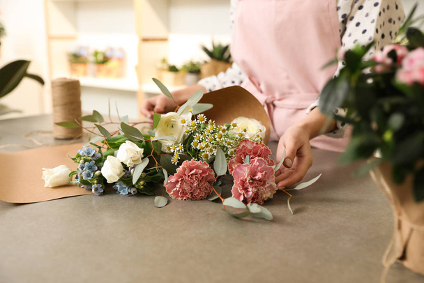 Florist making bouquet with fresh flowers at table, closeup - 写真・画像