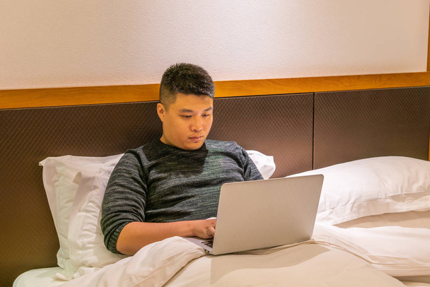 Young businessman using laptop on bed in the business travel - Foto, Imagem