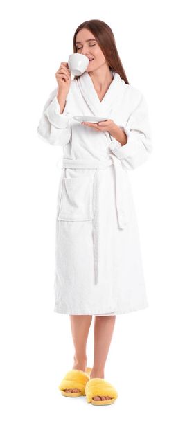 Young woman in bathrobe with cup of drink on white background - Foto, Imagen
