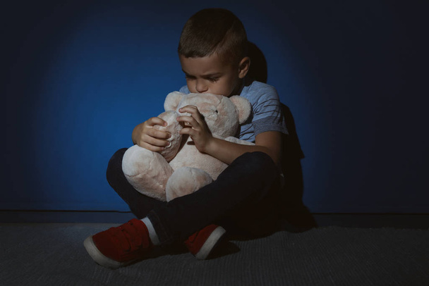 Niño triste con oso de peluche cerca de la pared azul. Violencia doméstica
 - Foto, Imagen